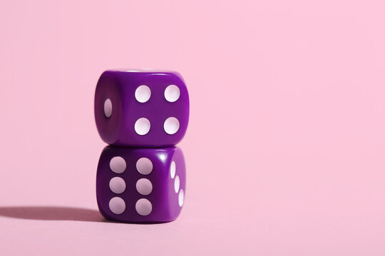 Purple game dices on pink background, closeup
