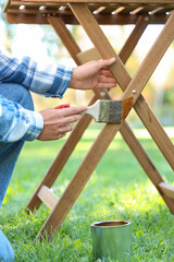 Woman painting wooden table in garden, closeup
