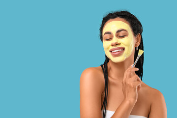 Fototapeta premium Young African-American woman with turmeric mask on her face against blue background