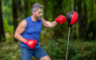 Sportsman boxing freestanding punching bag outdoor. Sport man boxing punching bag. Strong athlete man boxer. Boxer in sportswear. Exercising and punching. Sportsman practicing boxing