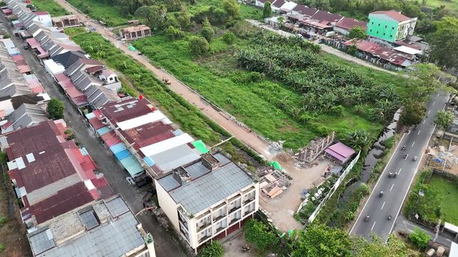 Aerial footage from a drone shows a suburban residential area with rows of closely packed houses and a main road with vehicles under a clear sky.
