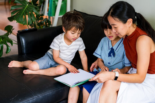 Two children eagerly explore a storybook with an attentive adult on a couch