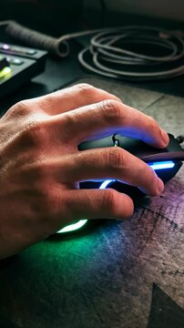 Close up of a hand using an illuminated RGB gaming mouse on a dark textured pad at a computer workstation