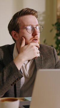 Thoughtful young professional man with glasses working at laptop, transitioning from stress and worry to calm focus while concentrating in cozy home office