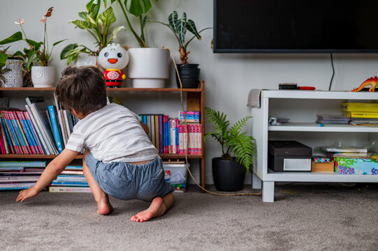 Young child squats down to explore colourful books on a shelf in a comfortable living space