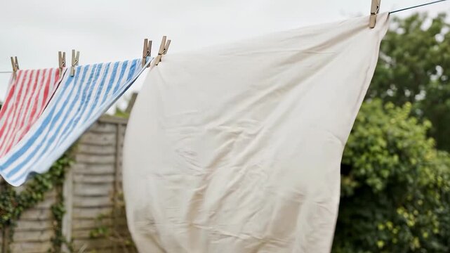 White sheet and striped towels hanging on a clothesline outdoors blowing in the wind on a cloudy day