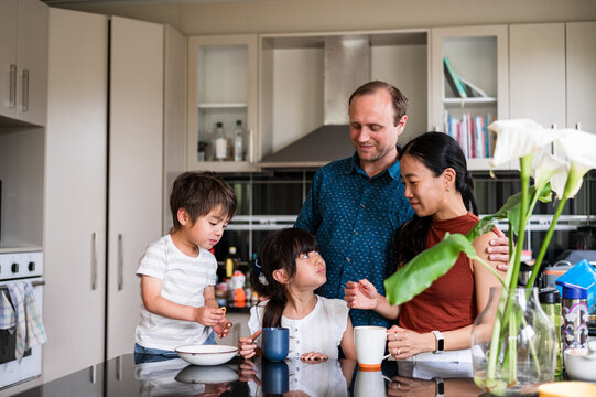 Parents and their two young children share breakfast and smiles in a modern kitchen setting.