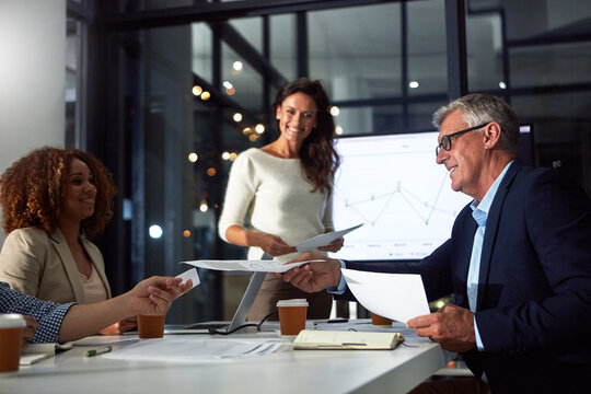 People, presentation and paperwork in office at night with finance report, data analysis and profit. Mature man, team and documents for sales growth, audit graphs and overtime for performance metrics