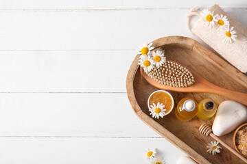 Spa composition with tray, massage body brush and bottles of chamomile essential oil on white...