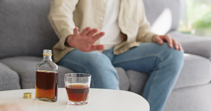 Man displays refusal to alcohol drink sobriety. He rejects a bottle on the table, stressing addiction risk, recovery focus and health goals at home. Clear message: no alcohol, choose health.