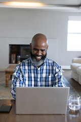 Naklejka premium Mature African American man plaid-shirt sitting at table using silver laptop phone in living room