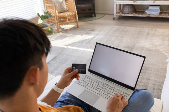 Laptop and credit card are resting on couch in living room with sunlight stripes from blinds