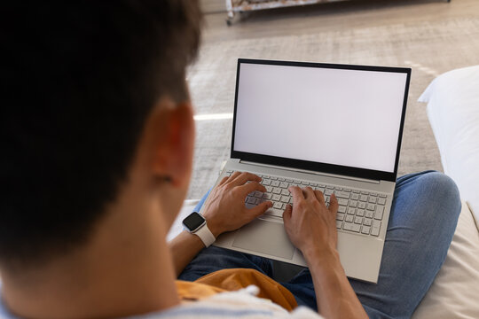 Open laptop sitting on lap of seated person on bed, smartwatch and bedding visible