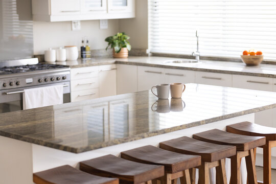 Polished granite island showing two mugs, five stools, range hanging towel, blinds streaming light