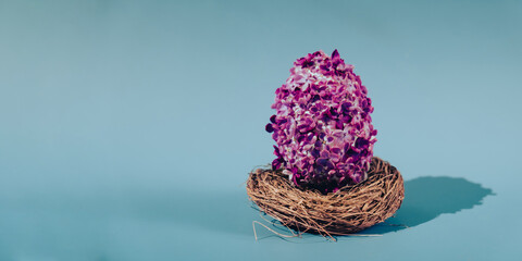 Easter egg made of lilac spring flowers in pastel blue background. Sustainable holiday minimalistic...