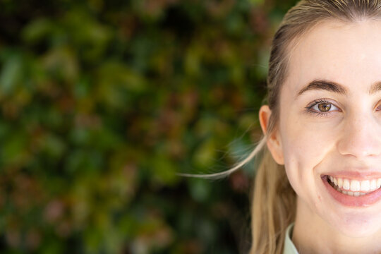 Female smiling with dimple and ponytail, posing outside near hedge in collared top, copy space