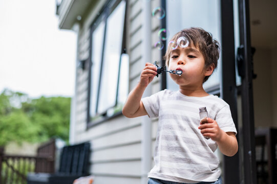Young boy enjoys blowing bubbles with a bubble wand outside a home