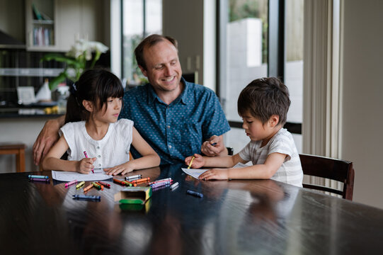 Two kids and an adult happily draw together at the dining table