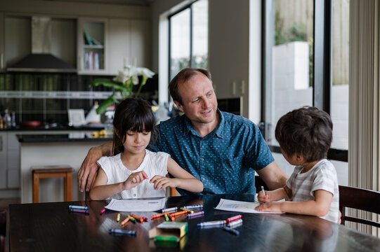 A father enjoys quality time with his kids drawing at the kitchen table