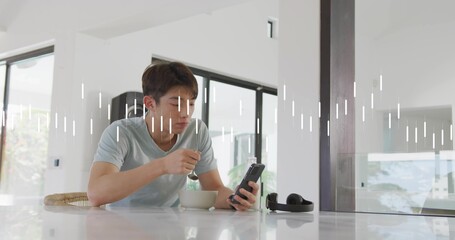 Obraz premium Eating teen male wearing light grey tee, leaning at modern kitchen counter, holding phone and bowl