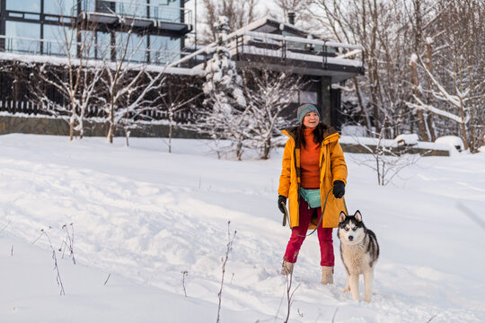 Asian woman walks in the snow with her husky dog in winter.