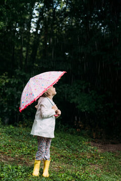 Side view of child holding colorful umbrella in rain shower