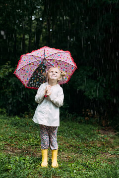 Happy little girl holding a colorful umbrella in the rain