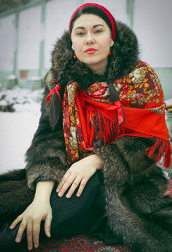 A woman with braids wearing a red kokoshnik, a pscarf and a fur coat