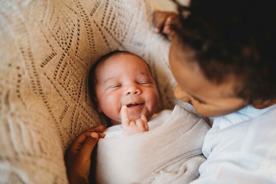 Multiracial boy kissing hugging smiley newborn baby in bed
