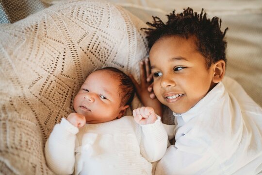Multiracial boy kissing hugging smiley newborn baby in bed