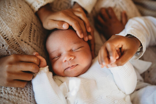 Multiracial newborn baby boy with black siblings holding hands in bed