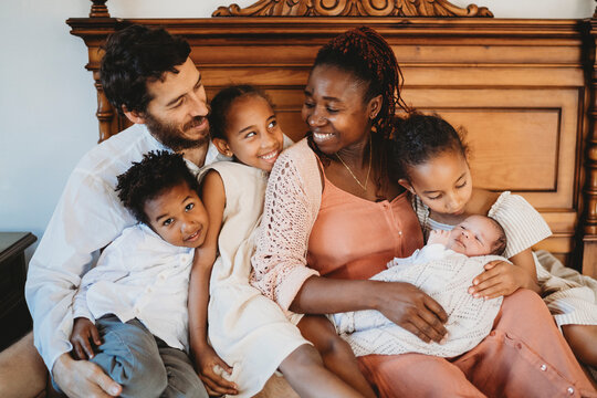 Multiracial family of six in bed black mom white dad smiling newborn