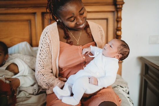 Black mom smiling holding multiracial newborn baby in bed