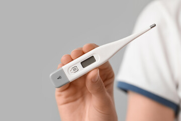 Woman with electronic thermometer on grey background
