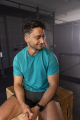 Obraz premium South Asian adult male sitting on plyometric box by pull-up rig in gym area, checking smartwatch