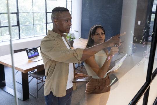 Diverse coworkers using tablet, collaborating at glass writing board in office, copy space - Powered by Adobe