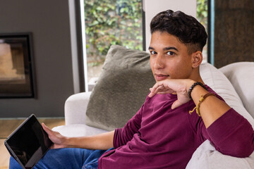 Naklejka premium Man sitting on light grey sofa holding tablet in living room with fireplace insert, windows