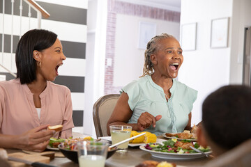 African American family laughing while eating at dining table with salad corn chicken lemonade