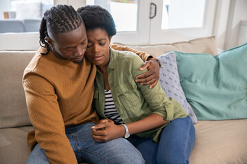 African american couple sitting on sofa at home with pillows and cushion, leaning contemplatively