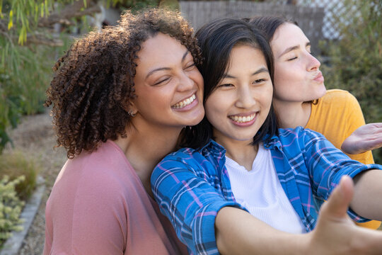 Diverse female friends posing for selfie in backyard garden while holding smartphone - Powered by Adobe