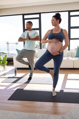 Obraz premium Diverse couple practicing yoga on mats with water bottle in living room overlooking waterfront view