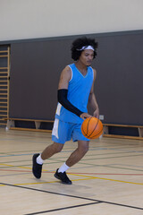 Obraz premium African american man dribbling basketball across court in gym wearing jersey