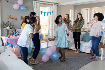 Obraz premium Diverse female friends celebrating baby shower in living room, dancing around pastel balloons