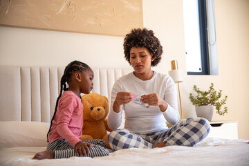 African american mother and daughter sitting on bed opening package with teddy bear in bedroom