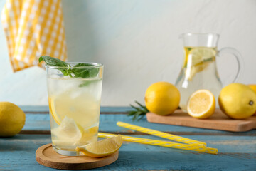 Fototapeta premium Glass of fresh lemonade with basil leaves and lemons on blue wooden table