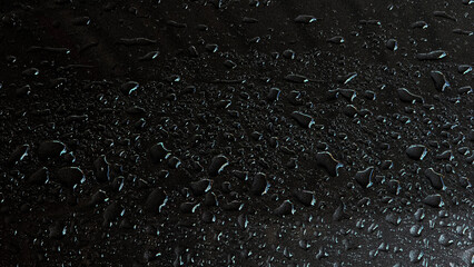 Sleek close-up shot of shimmering water droplets on dark textured metallic surface. Features moody...