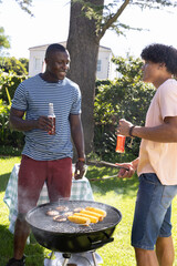 Diverse friends barbecuing burgers, corn on cob at grill in backyard near checkered table © wavebreak3