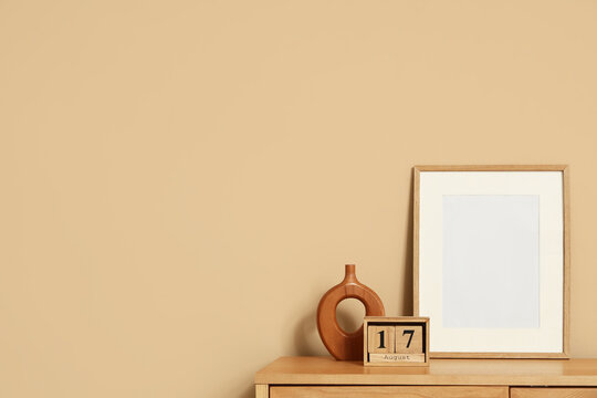 Cube calendar with date 17 AUGUST and blank frame on shelf near beige wall