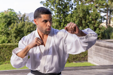 Man performing forward punch on wooden deck in garden wearing white gi and black belt