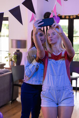 Diverse teenage friends snapping selfie with smartphone in living room with banners, balloons